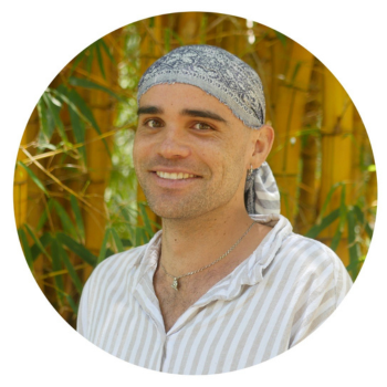 Smiling person wearing a headscarf and striped shirt, standing in front of bamboo plants.